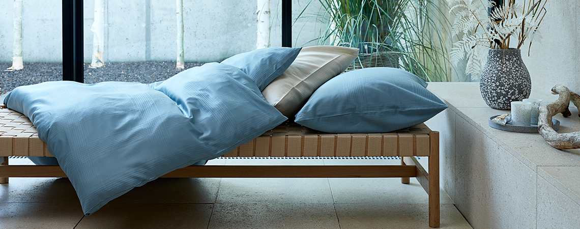 Biancheria da letto color petrolio su piumone e cuscino che copre un divano letto davanti a una finestra.