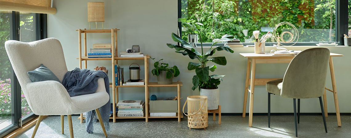 Poltrona grigia vicino a una finestra e un divisorio in bambù sullo sfondo. Lanterna di bambù sul pavimento accanto a una scrivania di bambù e una sedia da pranzo verde oliva