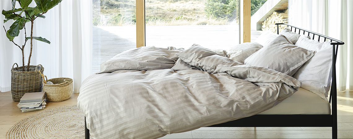 Camera da letto con letto in metallo nero, piumini e cuscini, rivestiti di lenzuola a righe in grigio chiaro e bianco. 