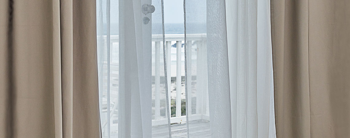 Vista su un balcone attraverso una porta aperta con tende mosse dal vento