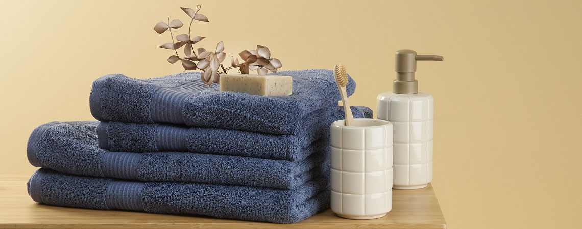 Pila di asciugamani blu su una panca con un portaspazzolino e un dispenser di sapone