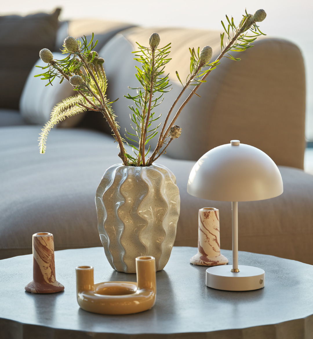 Portacndele, vasi e lampada in varie tonalità di beige su un tavolo lounge grigio