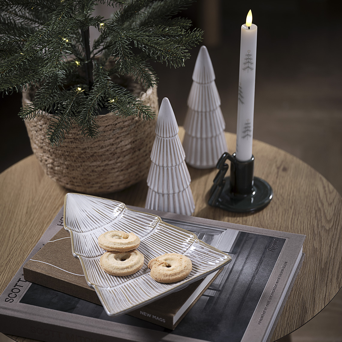 Vassoio decorativo con biscotti, due decorazioni a forma di albero di Natale e portacandela con candela su un tavolino 