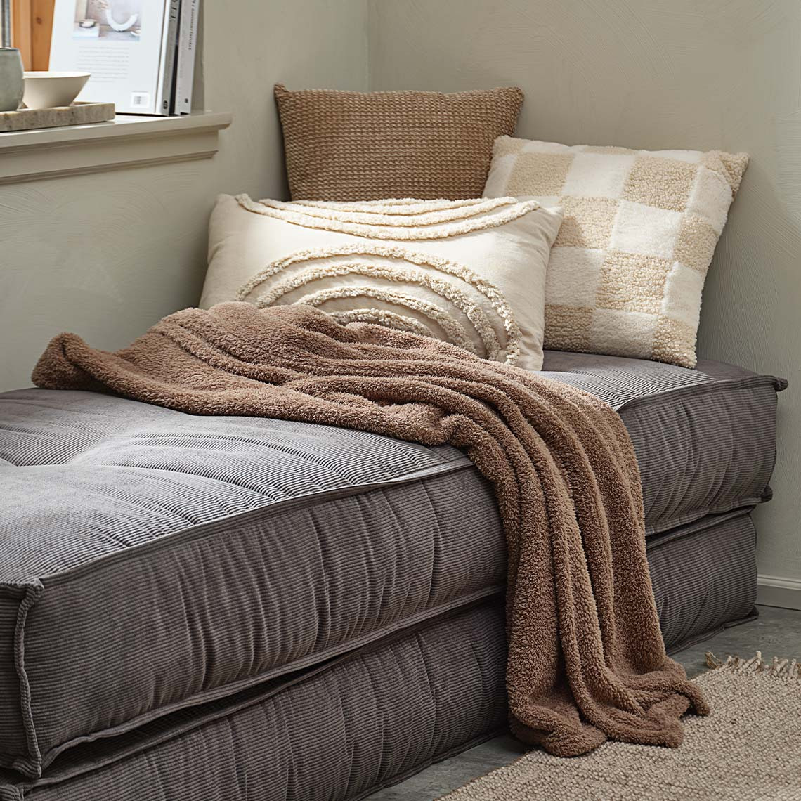 Coperta e cuscini decorativi in Mocha Mousse e beige su un divano letto