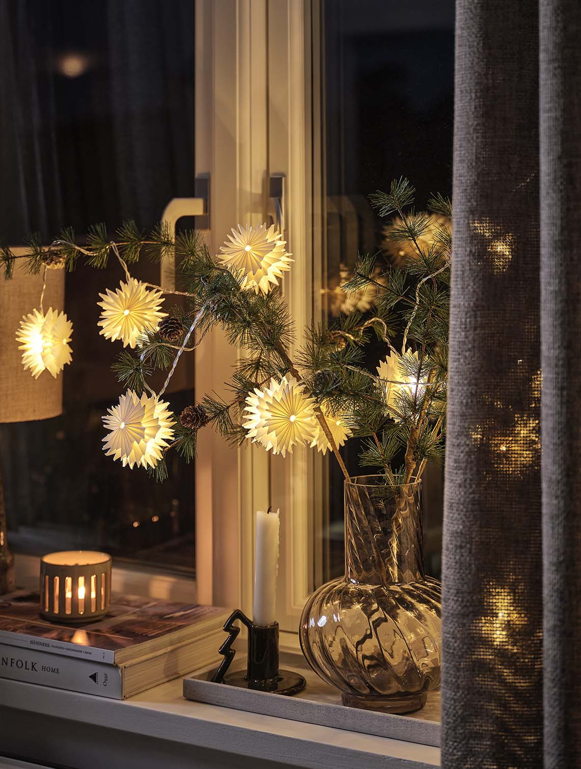 Catena di luci a forma di stella PLATIN con funzione timer Una catena di luci con decorazioni a forma di stella su un ramo di pino illumina il davanzale della finestra