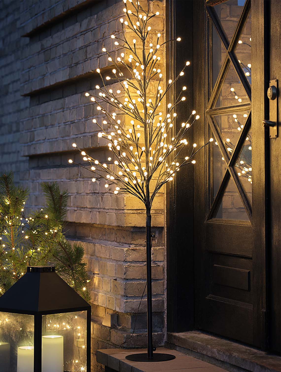 Albero luminoso NUNDORIT dotato di timer incorporato. Un albero luminoso a LED illumina la porta d’ingresso di una casa durante la notte
