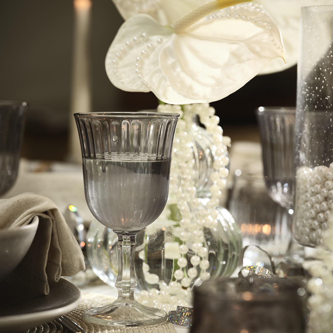 Un calice in vetro grigio su una tavoli imbandita con perle e fiori bianchi