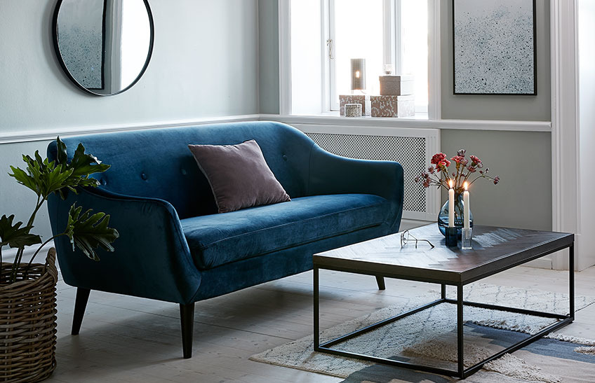 Un soggiorno con divano a due posti in velluto blu e un tavolino
