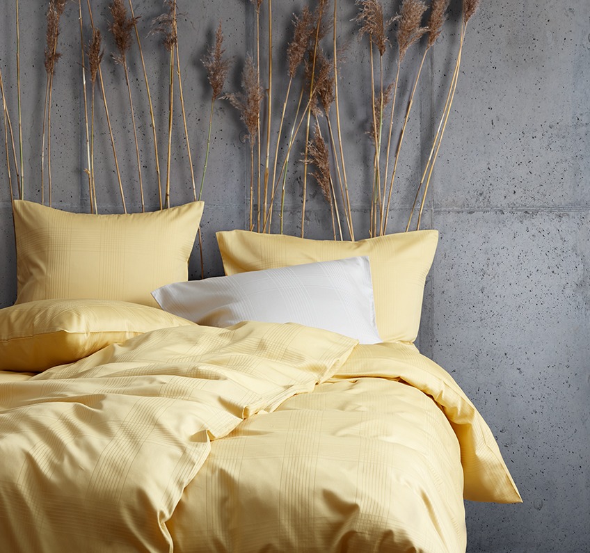 Biancheria da letto gialla in 51% poliestere riciclato e 49% raso di cotone in una camera da letto con pareti in cemento