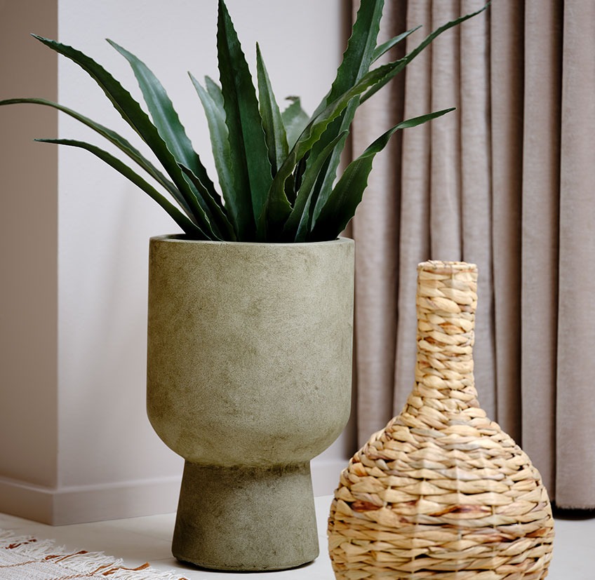 Vaso verde con pianta artificiale accanto a un vaso di vimini