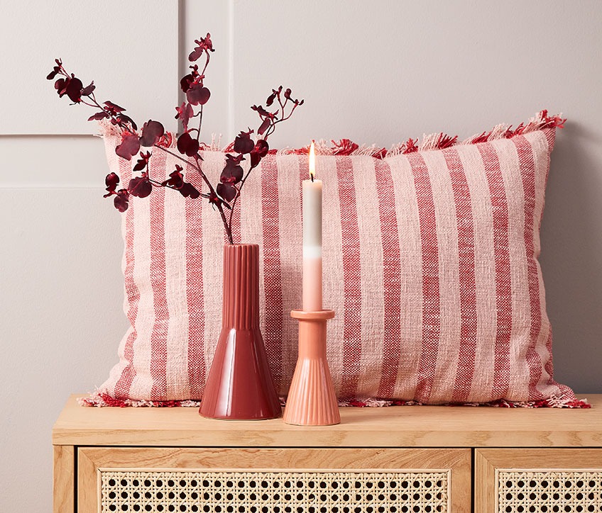 Cuscino a righe dietro vaso rosso e portacandela con candela a righe  
