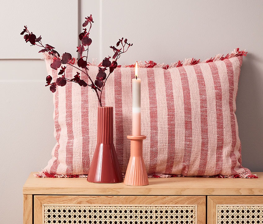 Cuscino DAGFIOL, fiori artificiali RAGNAR, vaso EGMUND e candeliere THRISTAN con candela IGNI Cuscino a righe dietro vaso rosso e portacandela con candela a righe