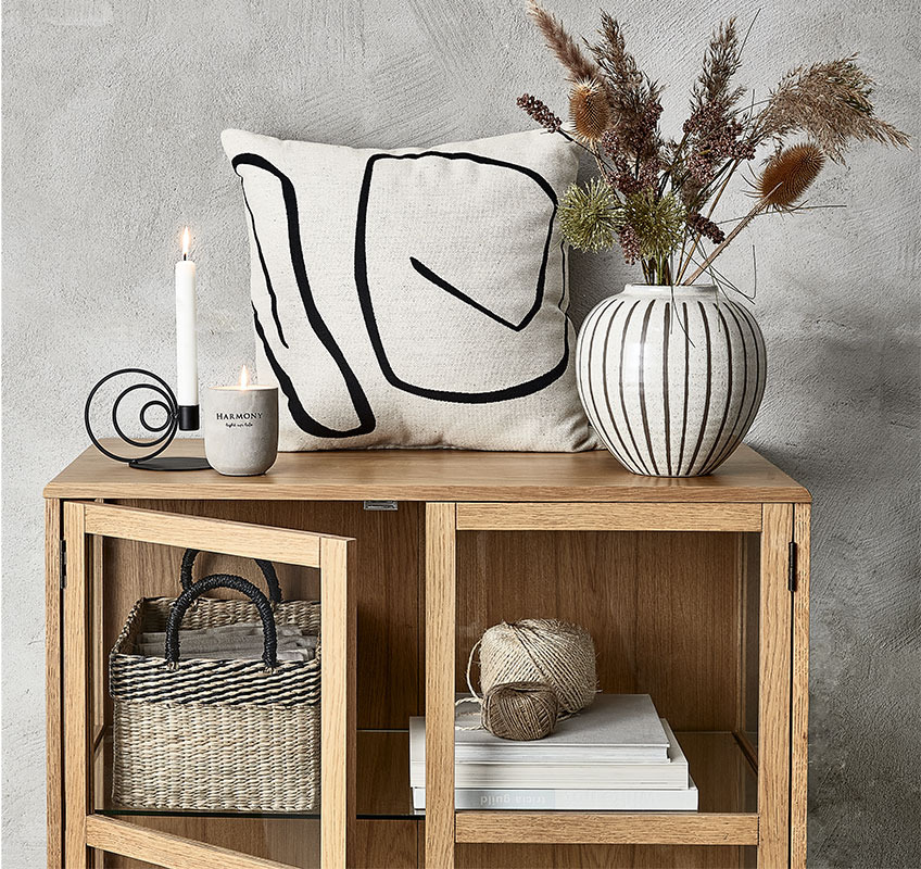 Coperta trapuntata, cuscini e vaso nei colori bianco, beige e grigio