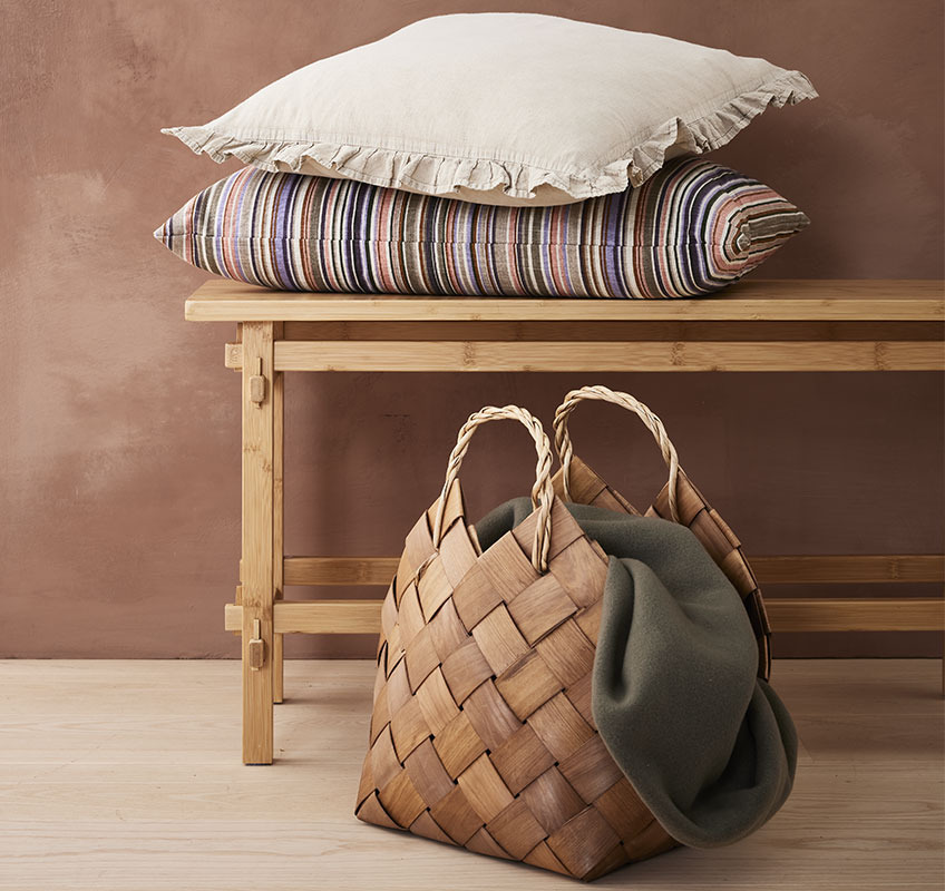 Decorative cushions on wood bench and basket with throw