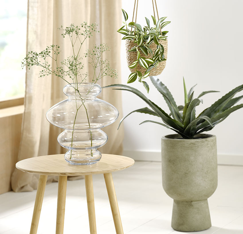 Vaso di vetro su un tavolino, vaso per piante sospese e vaso per piante verdi con piante artificiali