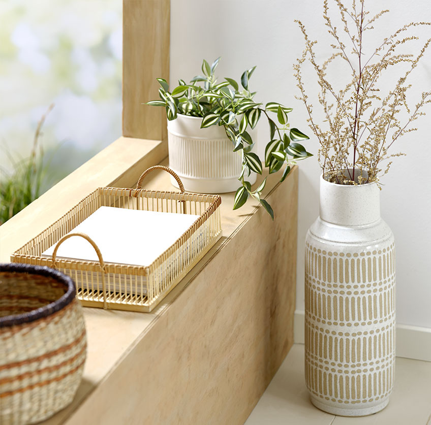 Vaso alto accanto al davanzale con vassoio di bambù e vaso bianco con pianta artificiale
