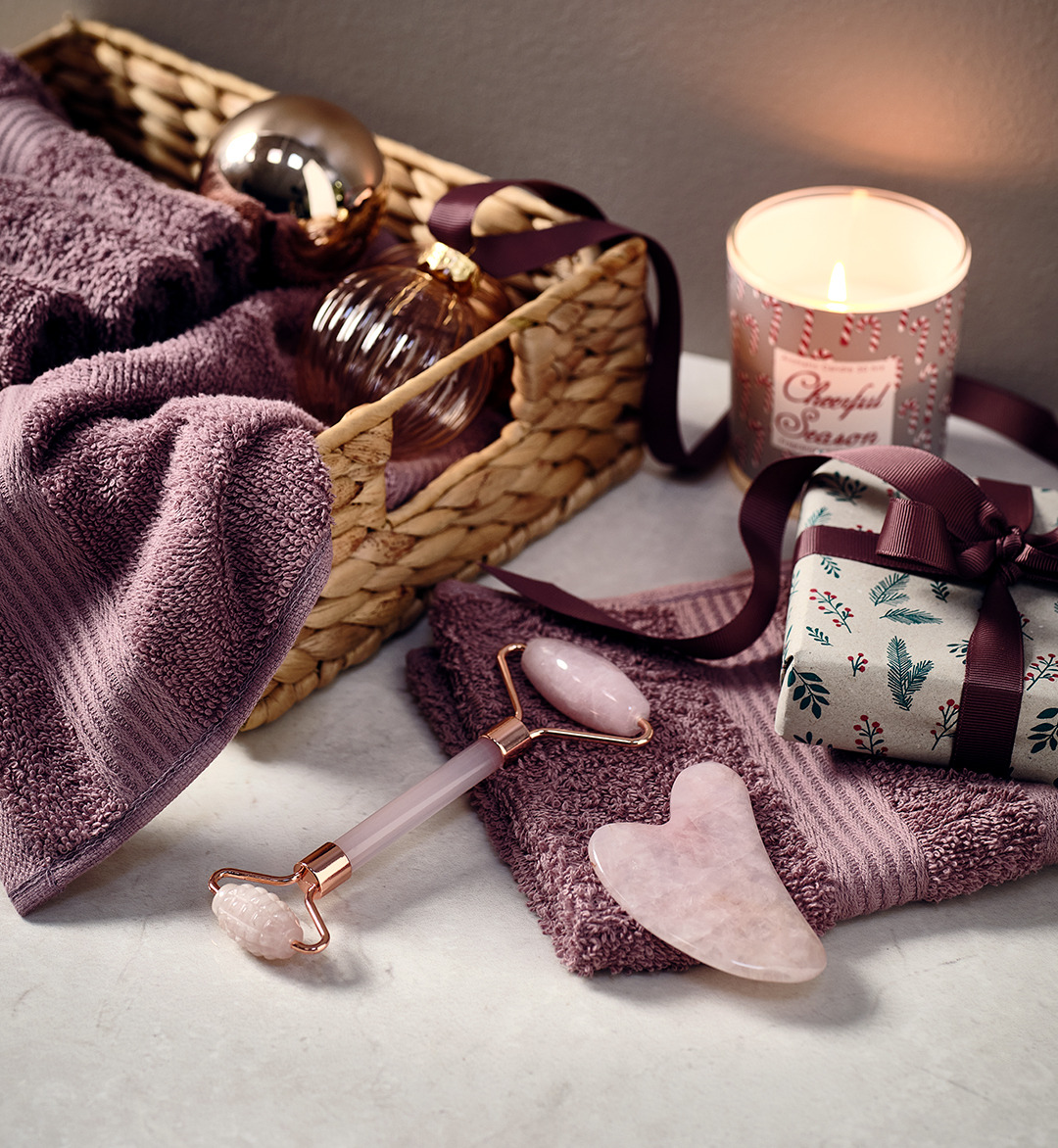 Rullo per il viso e accessorio massaggi color rosa, asciugamani color prugna e candela profumata