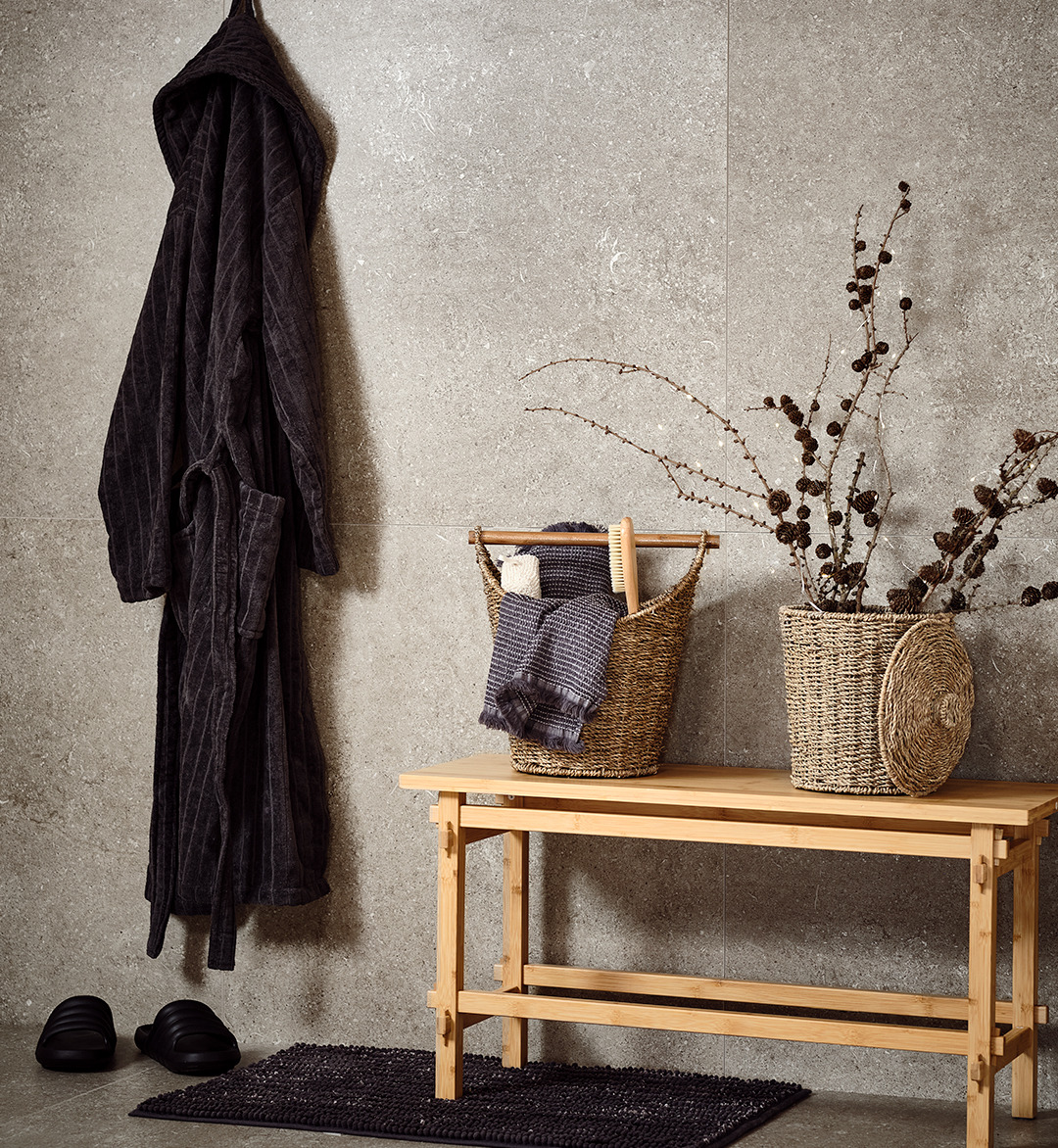 Accappatoio in cotone grigio, cesti e asciugamani su una panca in bambù