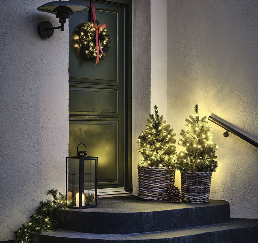 Due alberi con luci davanti alla porta d'ingresso e ghirlanda natalizia con fiocco rosso