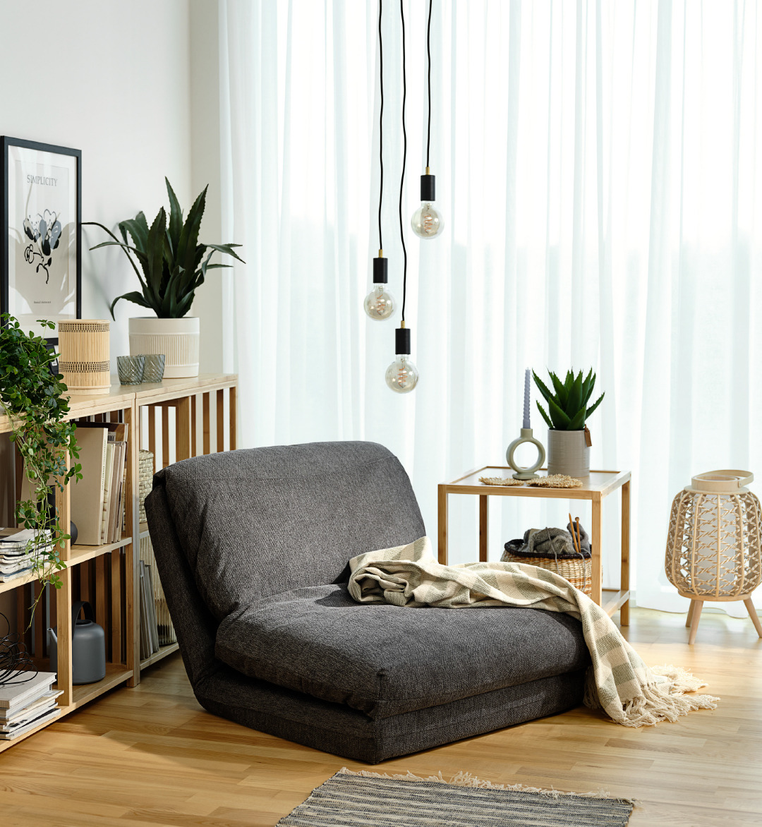 Poltrona letto VEGGER con lampadario MAGNAR e pianta artificiale CELIUS Angolo relax con poltrona grigia e accessori decorativi in stile naturale