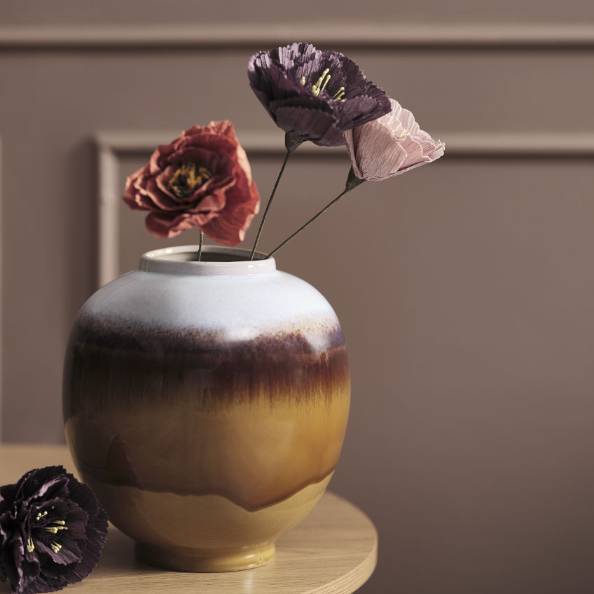 Vaso multicolore su tavolo con fiori artificiali rossi, viola e rosa