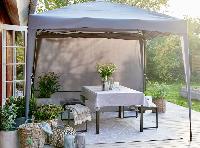 Gazebo grigio con tavolo e panche decorate e sistemate sul patio